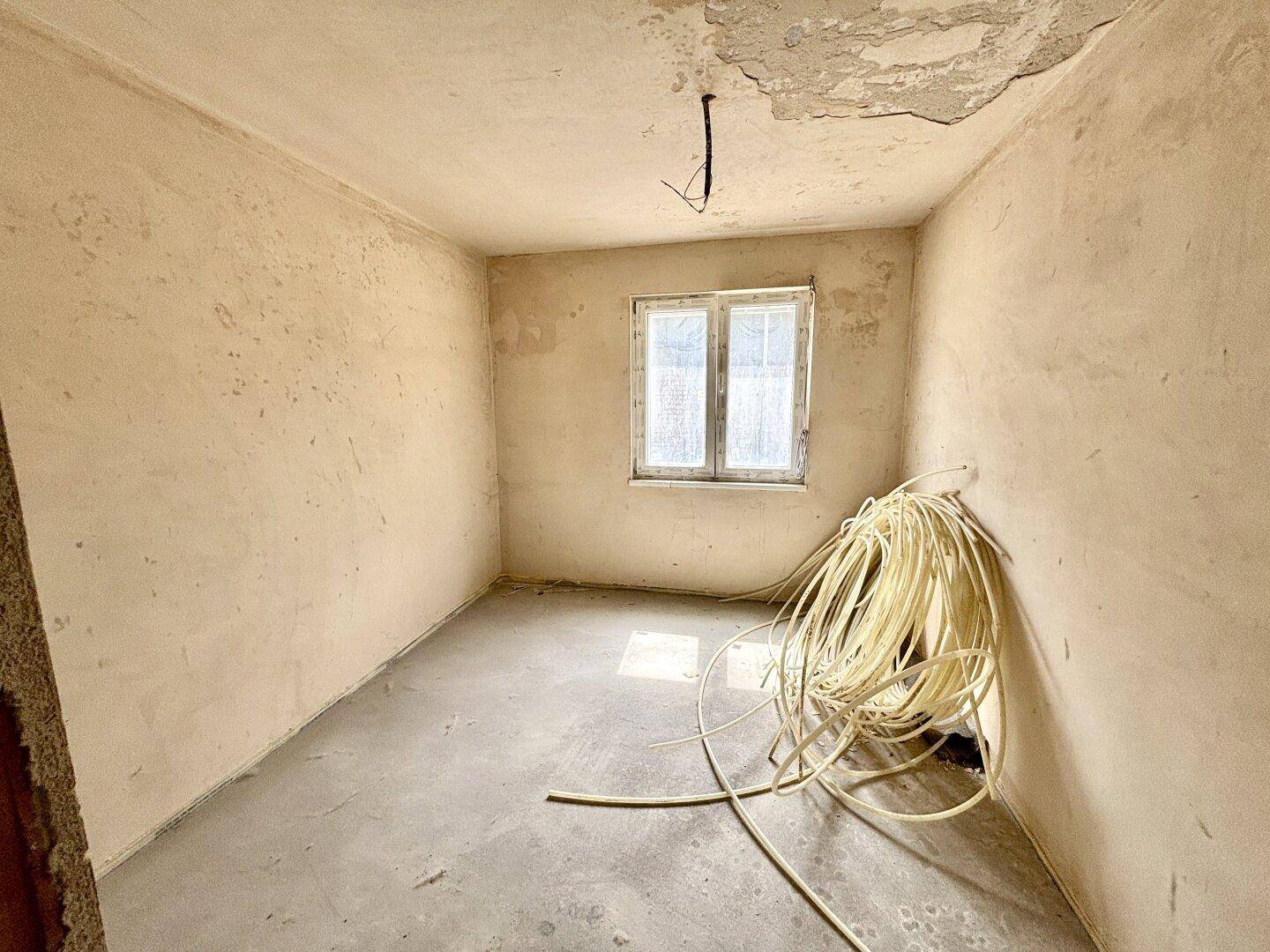 Kleiner, unfertiger Raum mit einem Fenster, geeignet als Schlaf- oder Arbeitszimmer.