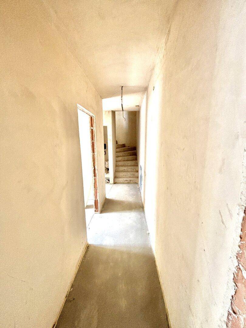 Langer, unfertiger Flur mit Blick auf eine Treppe im Hintergrund.