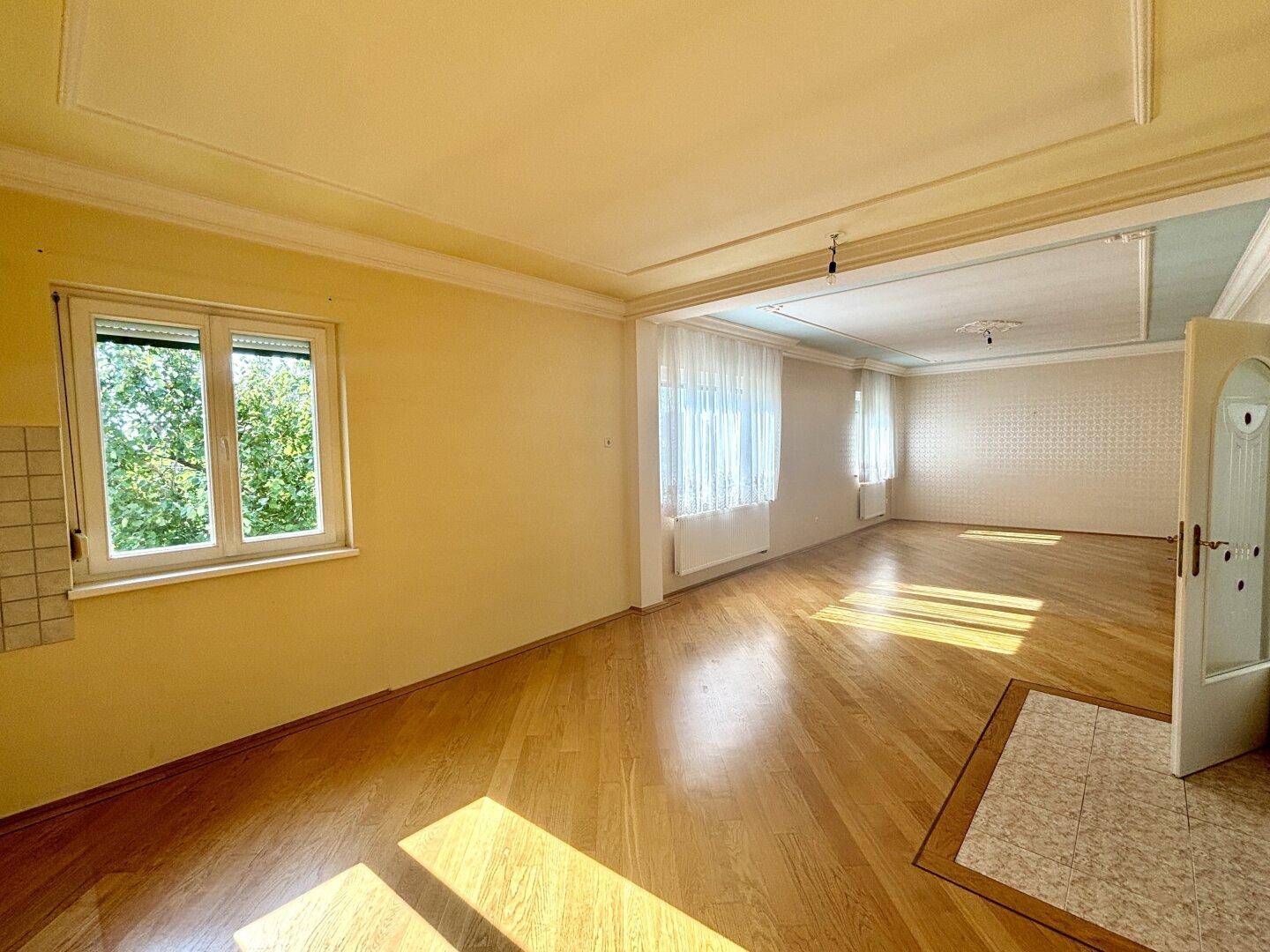 Helles und geräumiges Wohnzimmer mit Parkettboden, hohen Decken und Blick ins Grüne.