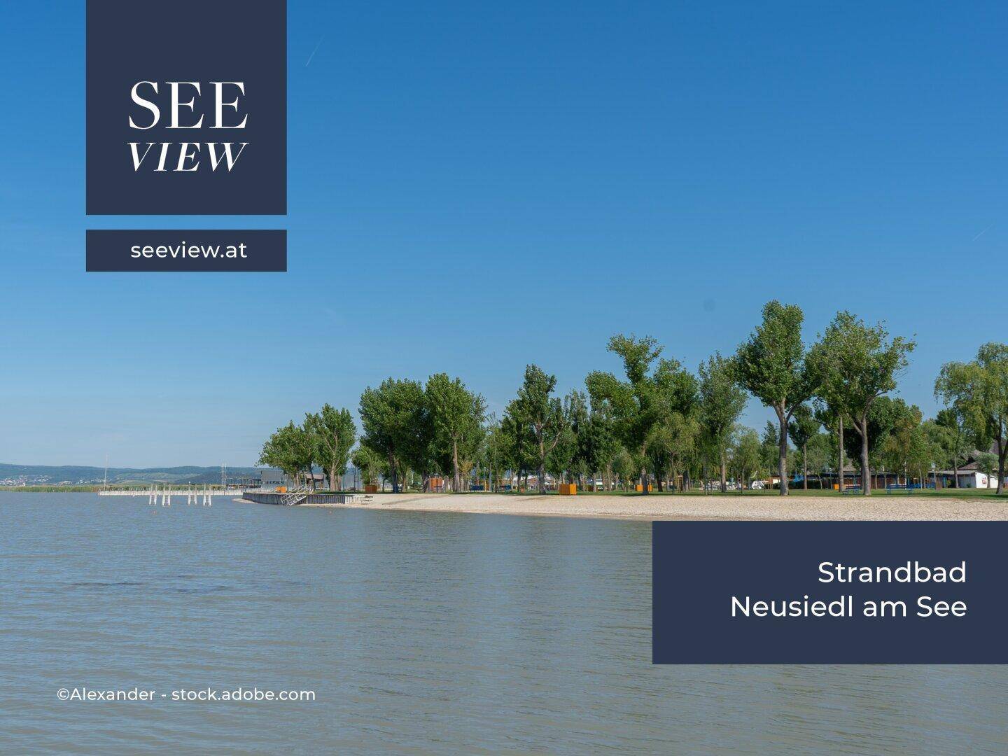 Das Strandbad Neusiedl am See mit Sandstrand, Bäumen und ruhigem Wasser an einem sonnigen Tag.