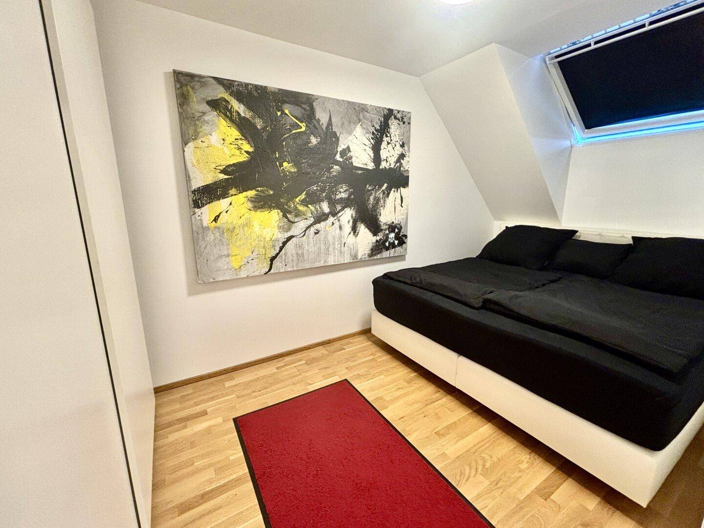 Schlafzimmer im Dachgeschoss mit Holzboden, großem Bett und abstraktem Wandbild.