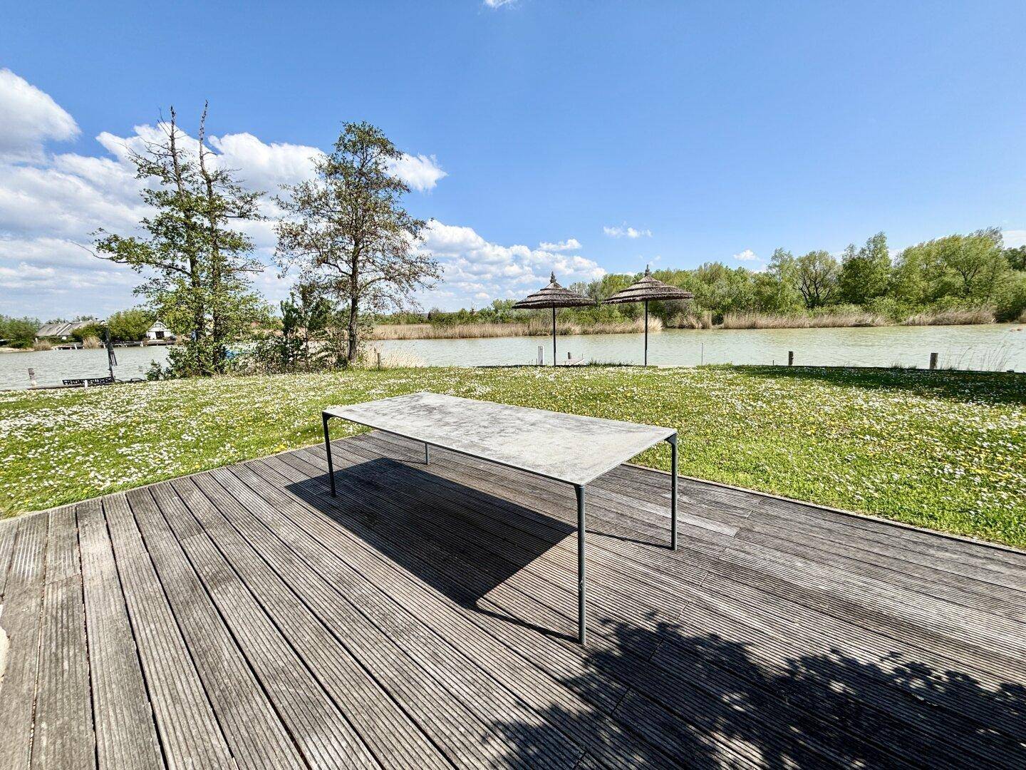 Holzterrasse mit Tisch und weitem Blick über den See und die grüne Landschaft.