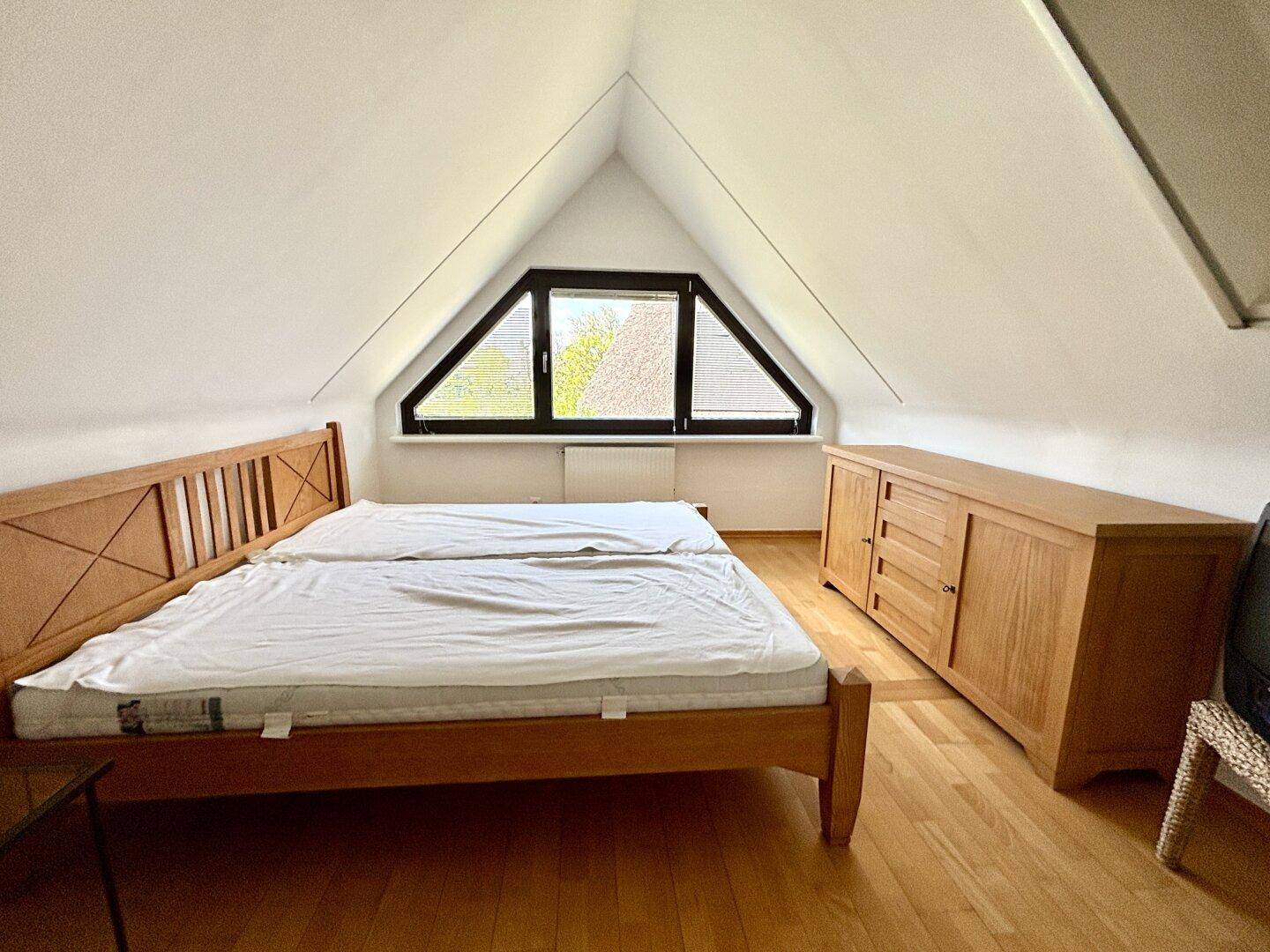 Helles Schlafzimmer im Dachgeschoss mit Holzboden, Holzmöbeln und schrägen Wänden.