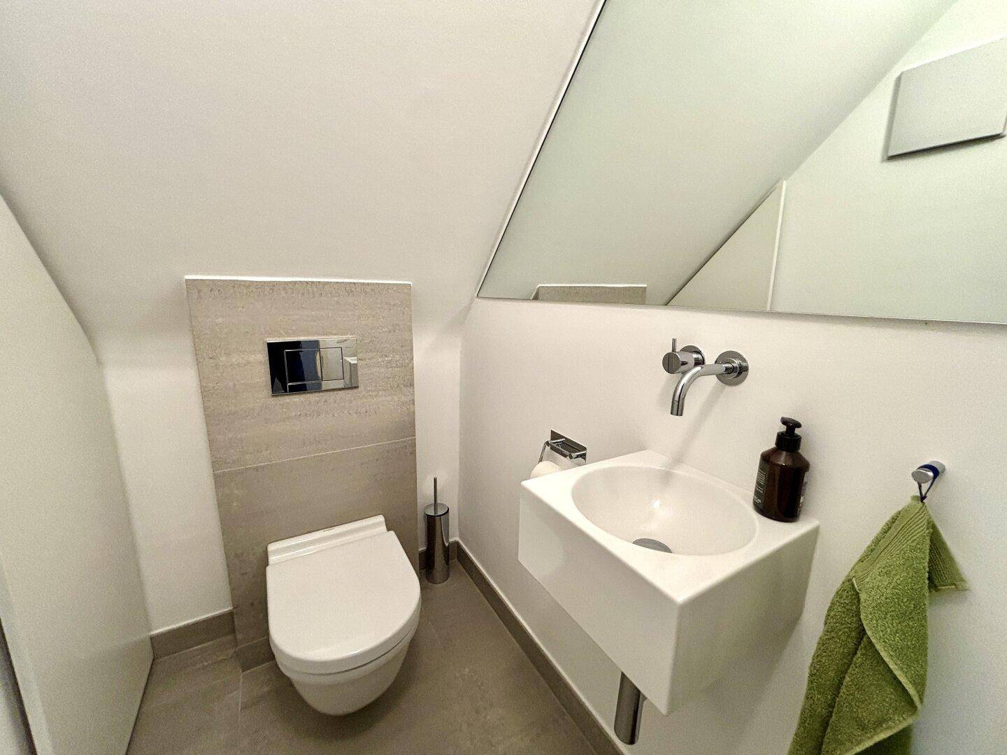 Modernes Gäste-WC mit wandhängender Toilette, kleinem Waschbecken und Spiegel.