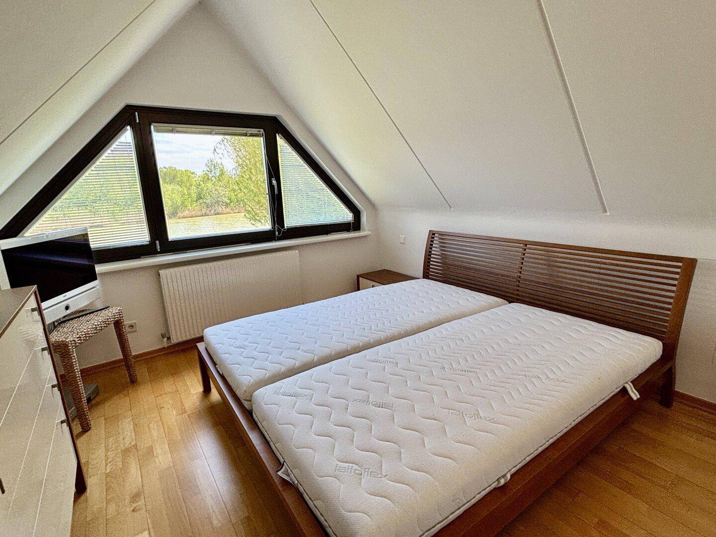 Schlafzimmer im Dachgeschoss mit Holzboden, Doppelbett und Blick auf die grüne Umgebung.
