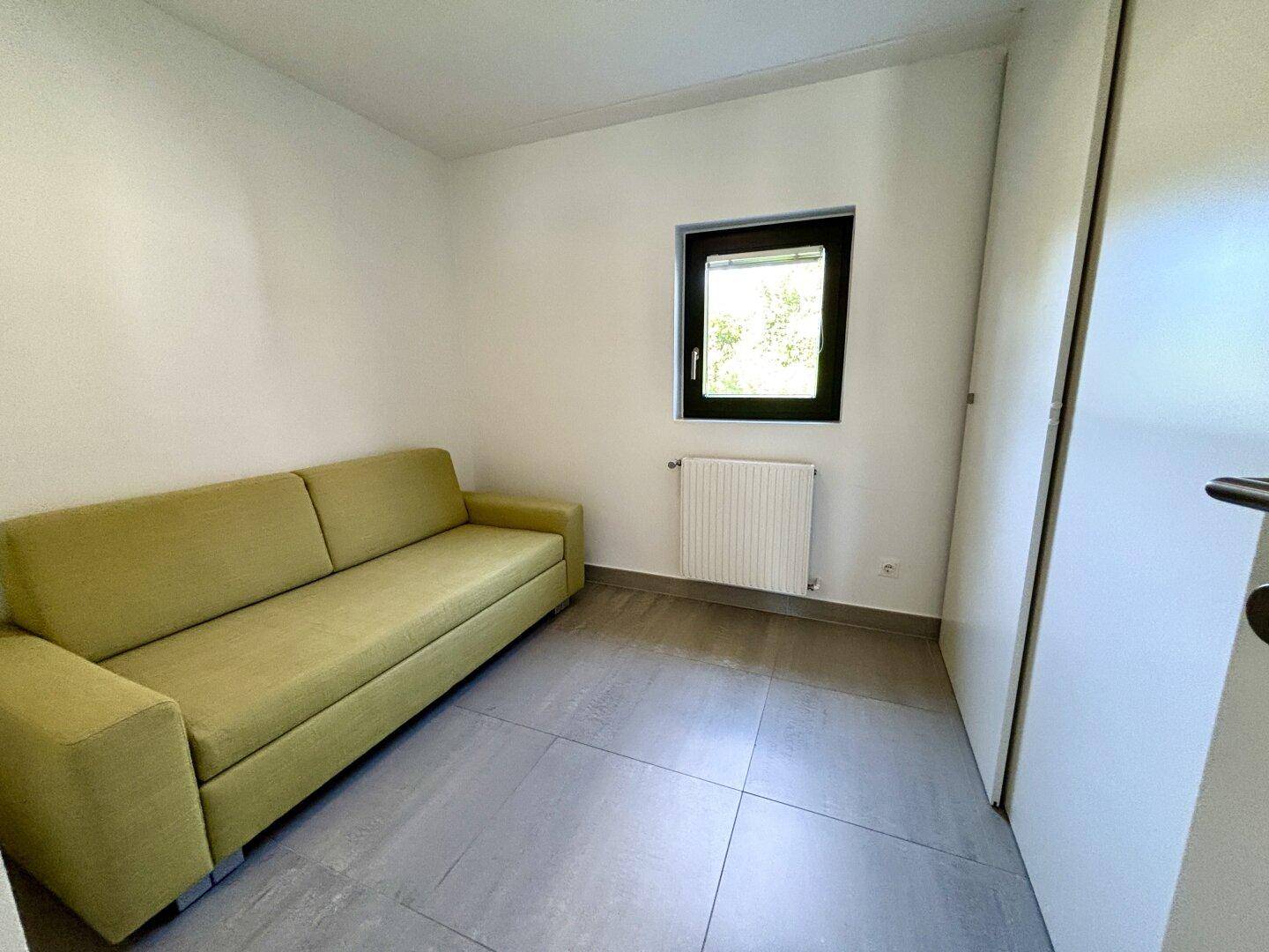Kleines Schlafzimmer mit Schlafsofa, Fliesenboden und einem Fenster für Tageslicht.