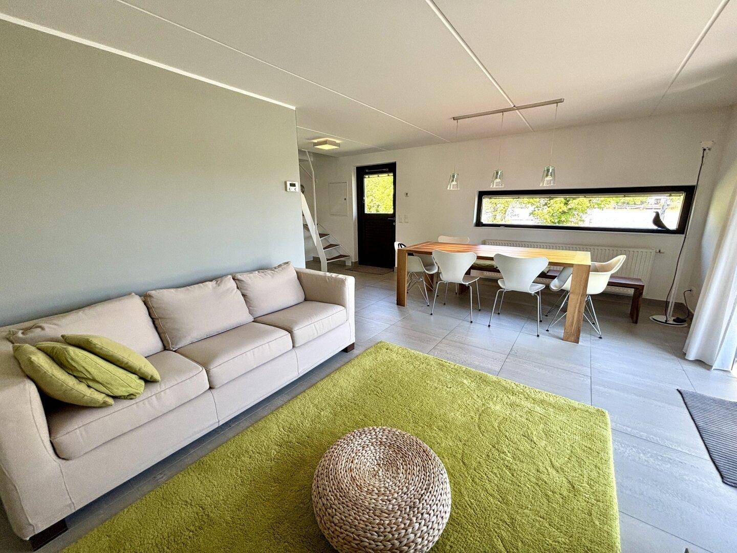 Geräumiger Wohn- und Essbereich mit beigem Sofa, Esstisch und Fliesenboden.