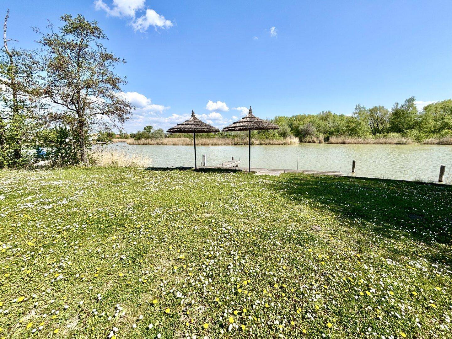 Großer Garten mit Rasenfläche, zwei Sonnenschirmen und direktem Zugang zum See.