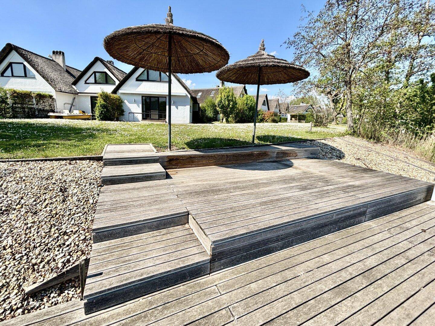 Holzterrasse mit Stufen und zwei Sonnenschirmen direkt am Seeufer gelegen.