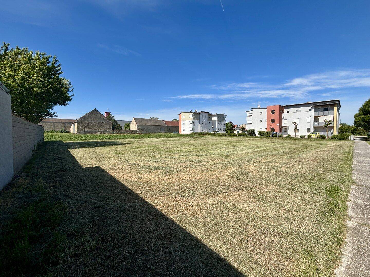 Großes, offenes Grundstück mit Gehweg und einer Mischung aus alten und neuen Gebäuden im Hintergrund.
