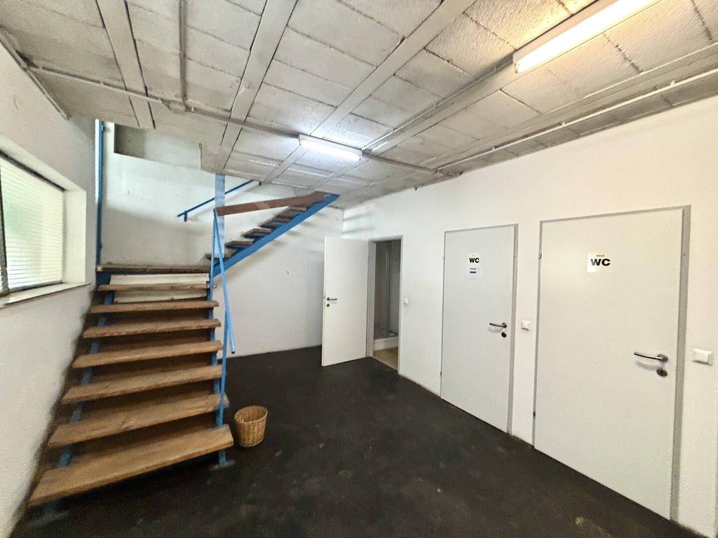 Flur mit Holztreppe, dunklem Boden und zwei Türen zu den Toiletten.