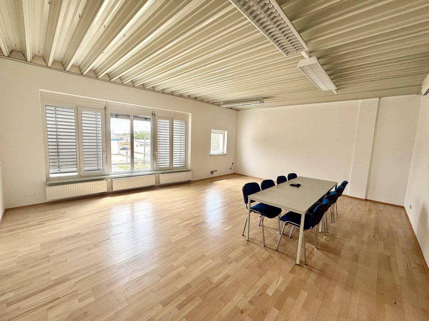Heller Büroraum oder Konferenzzimmer mit Holzboden, großem Fenster und Tisch mit Stühlen.