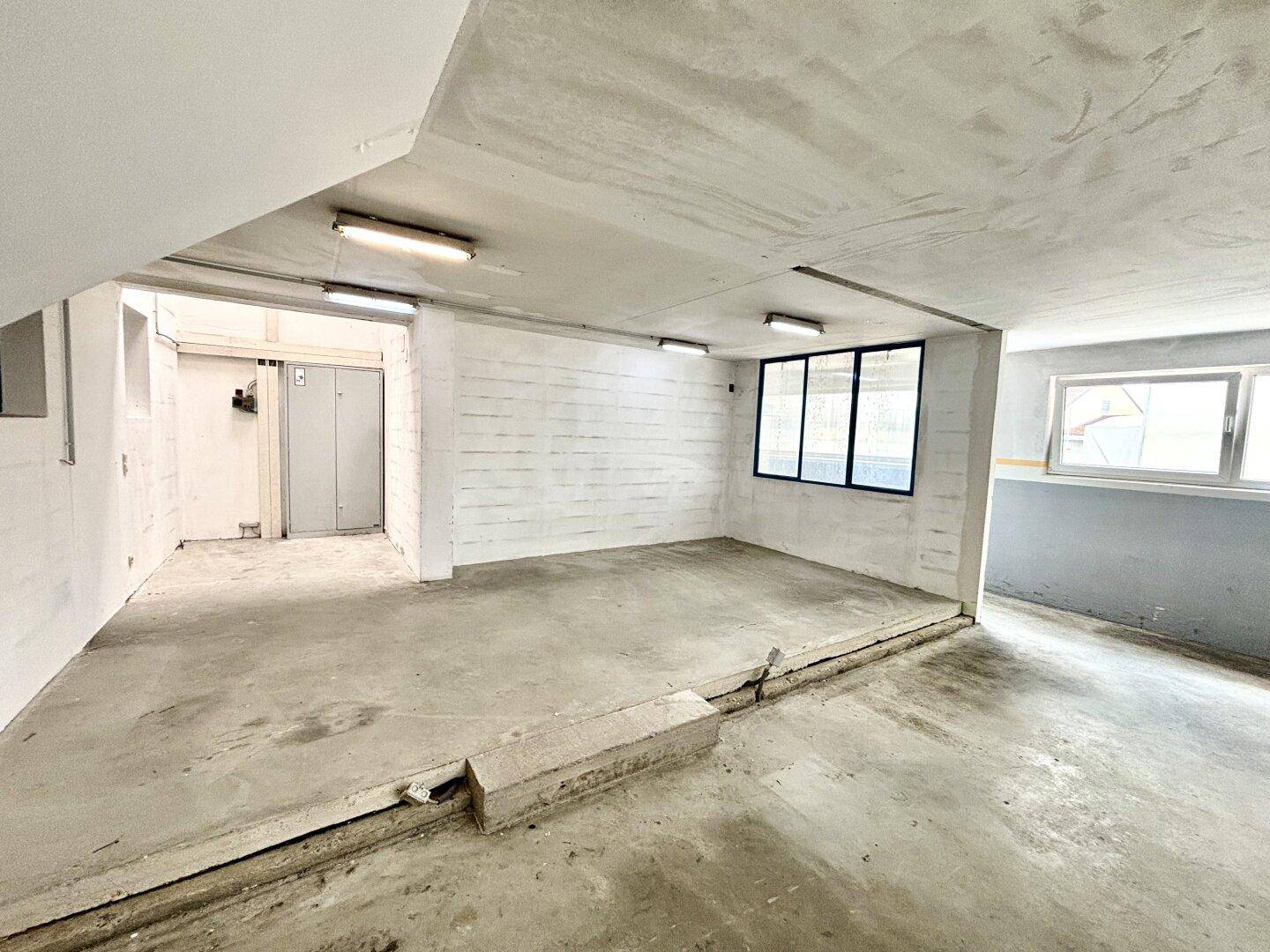Weiterer Blick in den leeren Gewerberaum mit Betonboden und Fenstern, ideal für verschiedene Nutzungen.