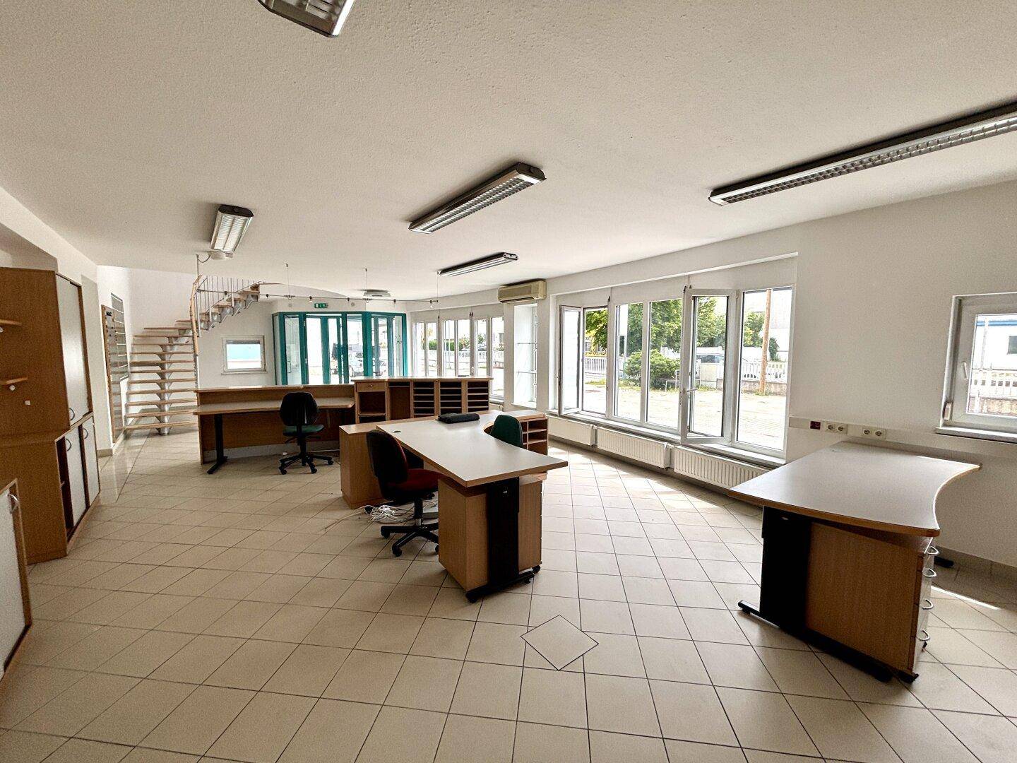 Großer Bürobereich oder Verkaufsraum mit Fliesenboden, Schreibtischen und viel Tageslicht.