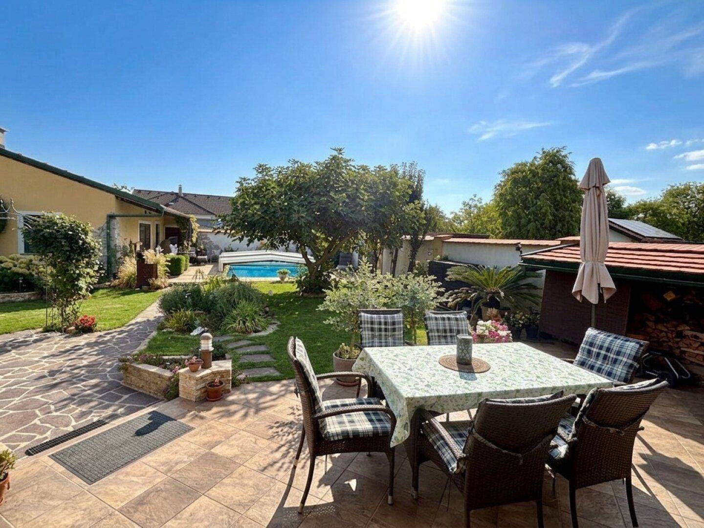 Sonniger Terrassenbereich mit Esstisch und Stühlen, Blick auf den Garten und den Swimmingpool.