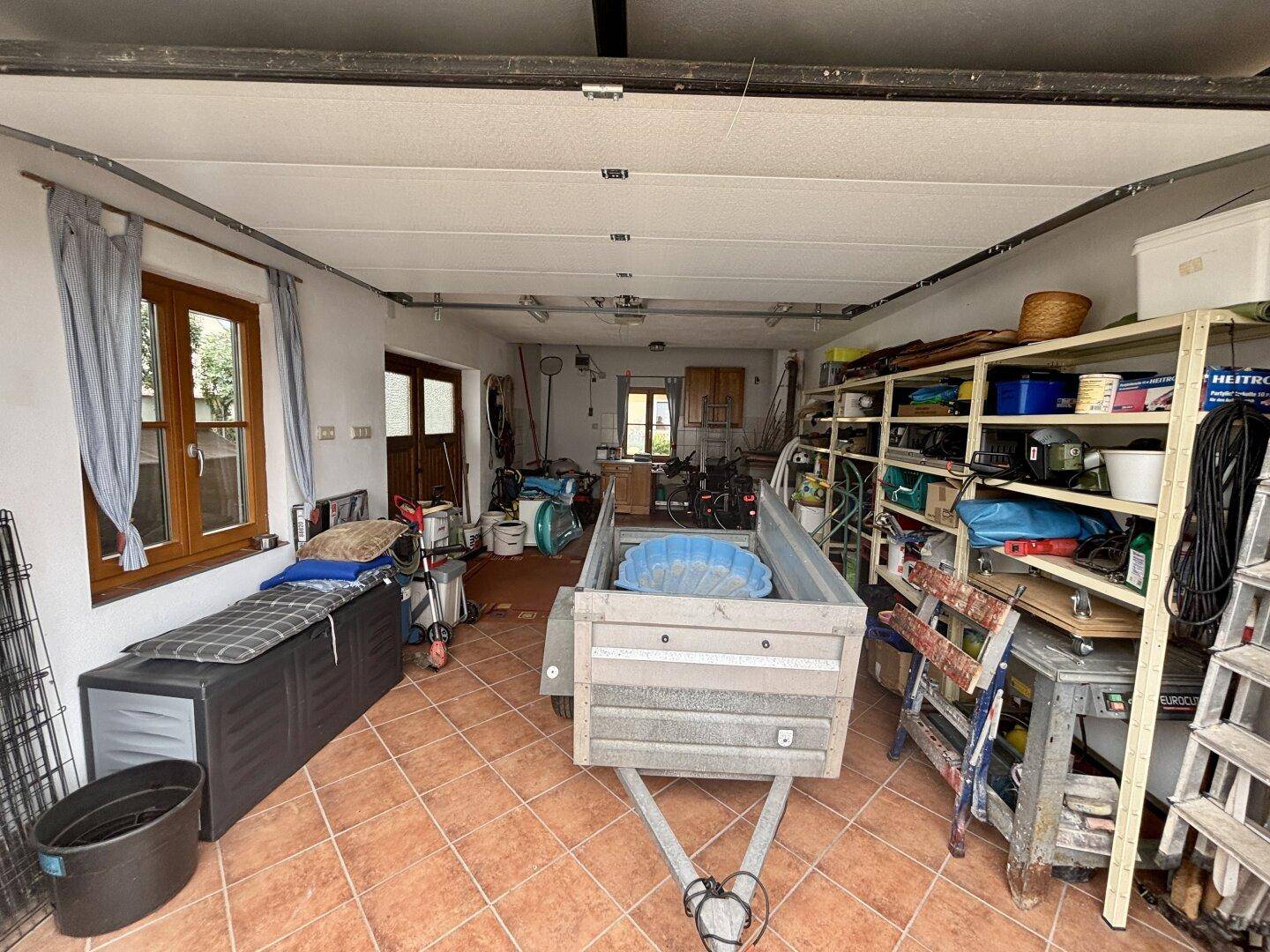 Geräumige Garage mit Fliesenboden, Fenstern und viel Stauraum für Werkzeuge und Geräte.