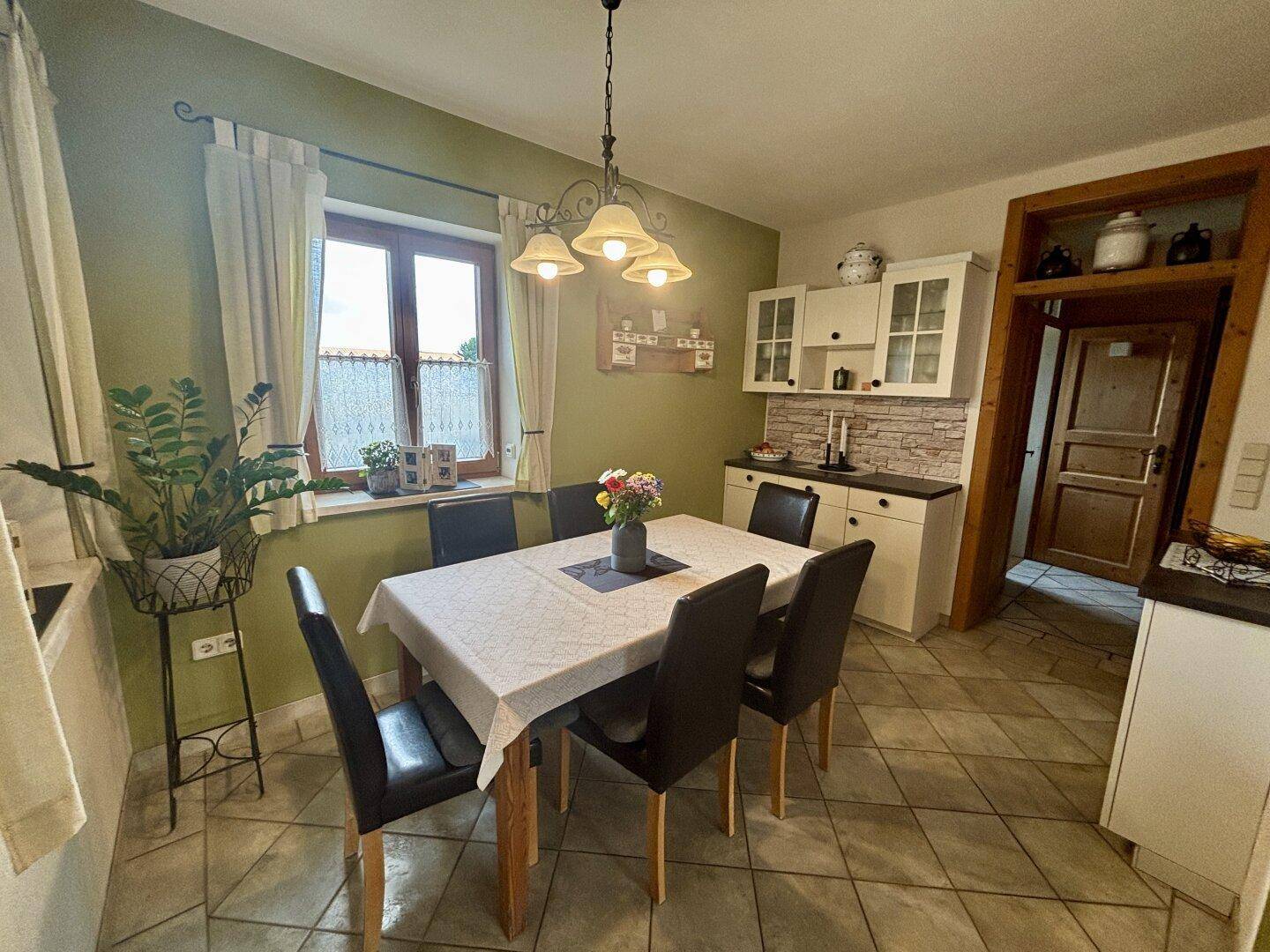 Heller Essbereich mit Holztisch, Stühlen und einer kleinen Küchenzeile im Hintergrund.