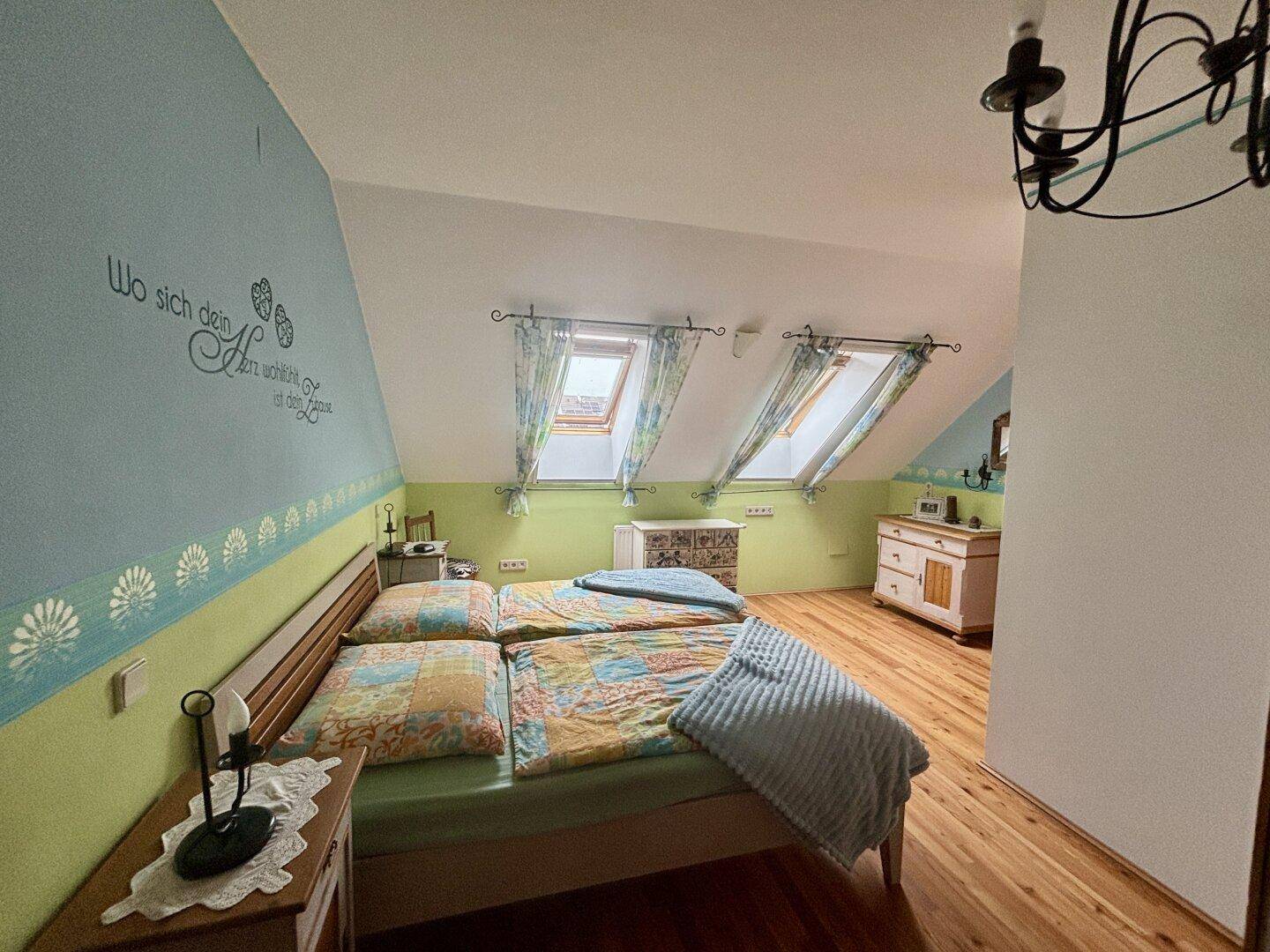 Gemütliches Schlafzimmer im Dachgeschoss mit Holzbett, Dachfenstern und farbigen Wänden.