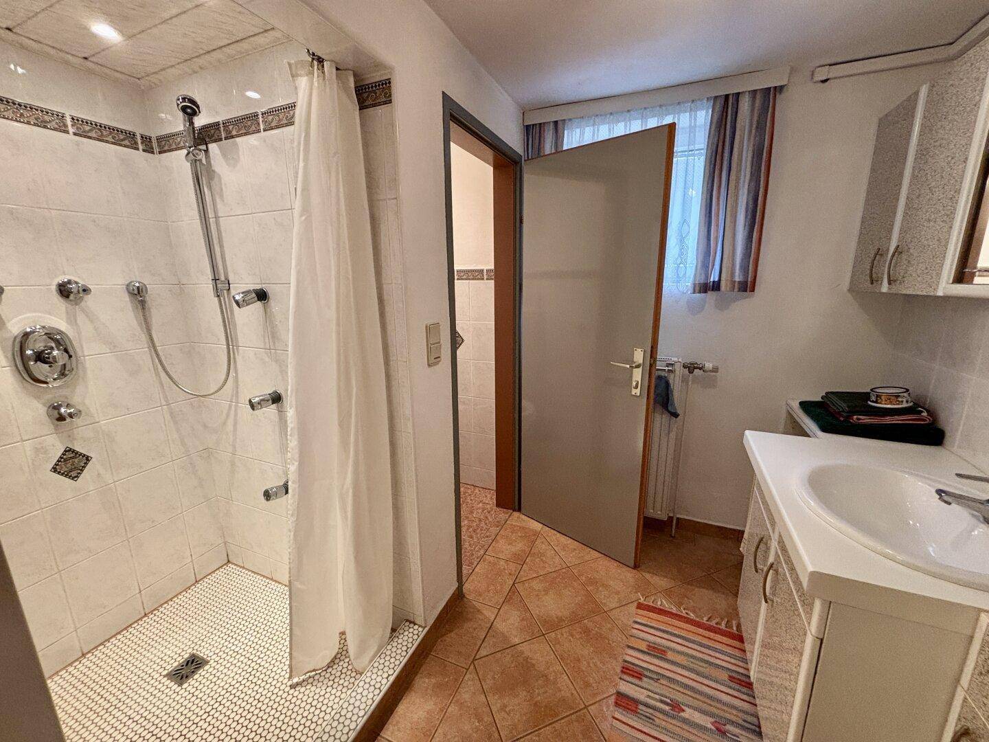 Kleines Badezimmer mit Duschkabine, Waschbecken und Fenster.