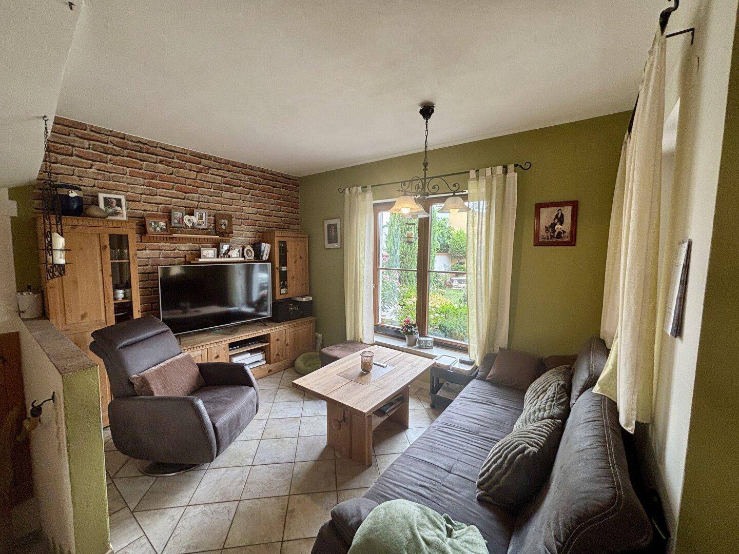 Wohnzimmer mit bequemer Couch, Fernseher und Blick in den grünen Garten.