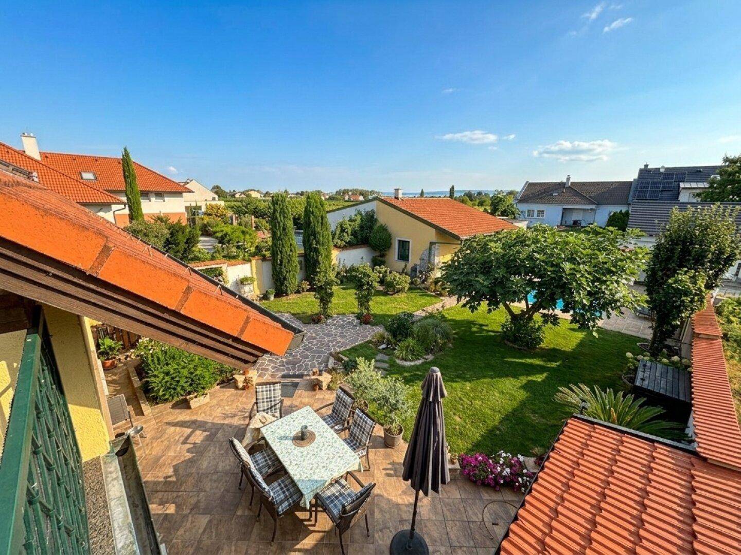 Panoramablick auf den weitläufigen Garten mit Pool, Terrasse und umliegenden Häusern.