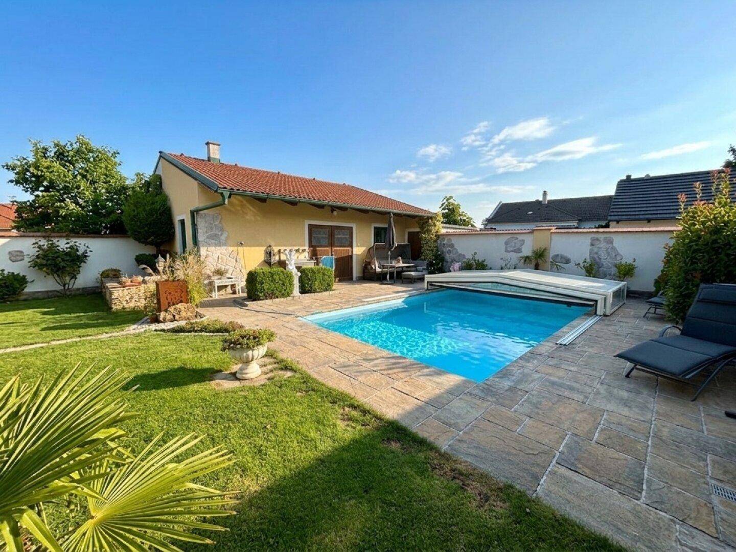 Sonniger Gartenbereich mit großem Swimmingpool, Liegestühlen und gepflegter Rasenfläche.