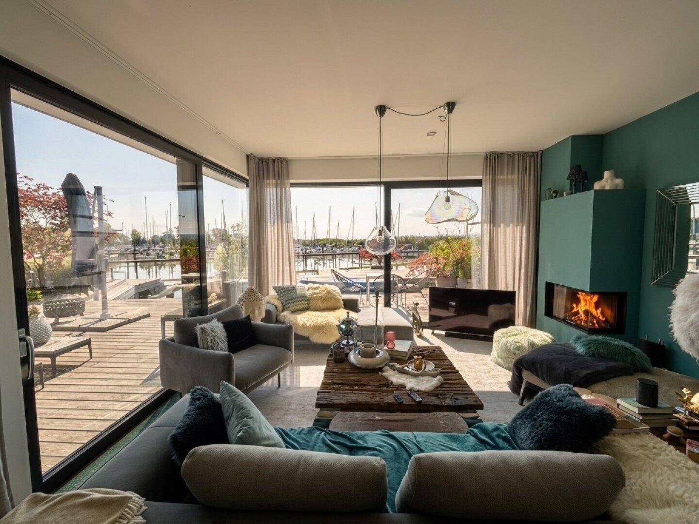 Helles Wohnzimmer mit Kamin, großen Fenstern und direktem Blick auf den Yachthafen.