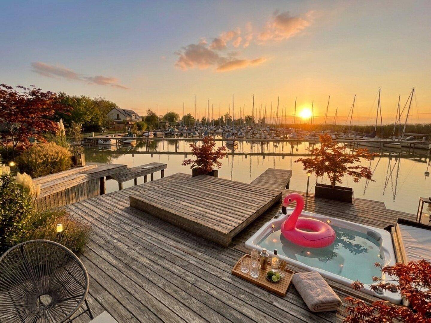 Gemütliche Holzterrasse mit Whirlpool und Blick auf den Yachthafen bei Sonnenuntergang.