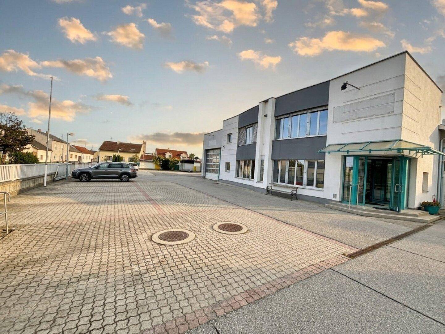 Außenansicht eines modernen Geschäftsgebäudes mit großem gepflasterten Parkplatz und klarem Himmel.