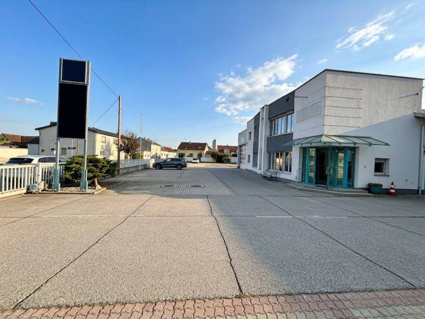 Weitläufiger Außenbereich eines Geschäftsgebäudes mit großem Parkplatz und einem markanten Werbeschild.