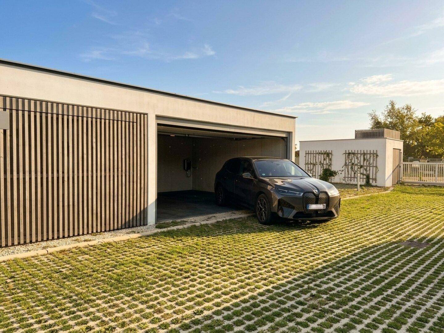 Moderne Garage mit einem Elektrofahrzeug und Rasengittersteinen im Vordergrund.