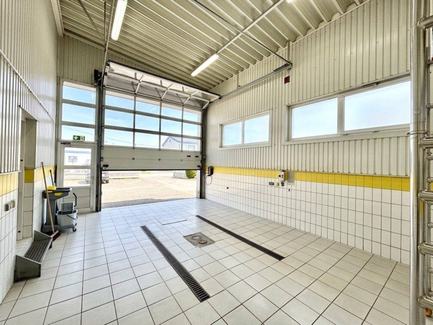 Helle und saubere Werkstatt oder Garage mit Fliesenboden, Rolltor und Entwässerungsrinnen.