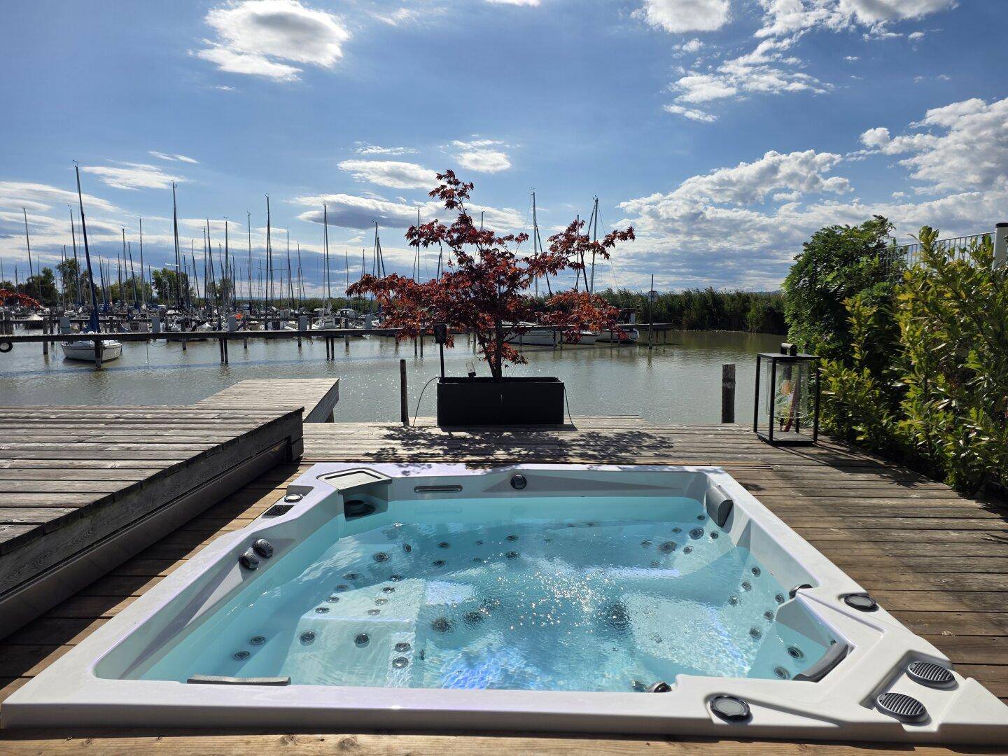 Luxuriöser Whirlpool auf einer Holzterrasse mit direktem Blick auf den See und den Yachthafen.