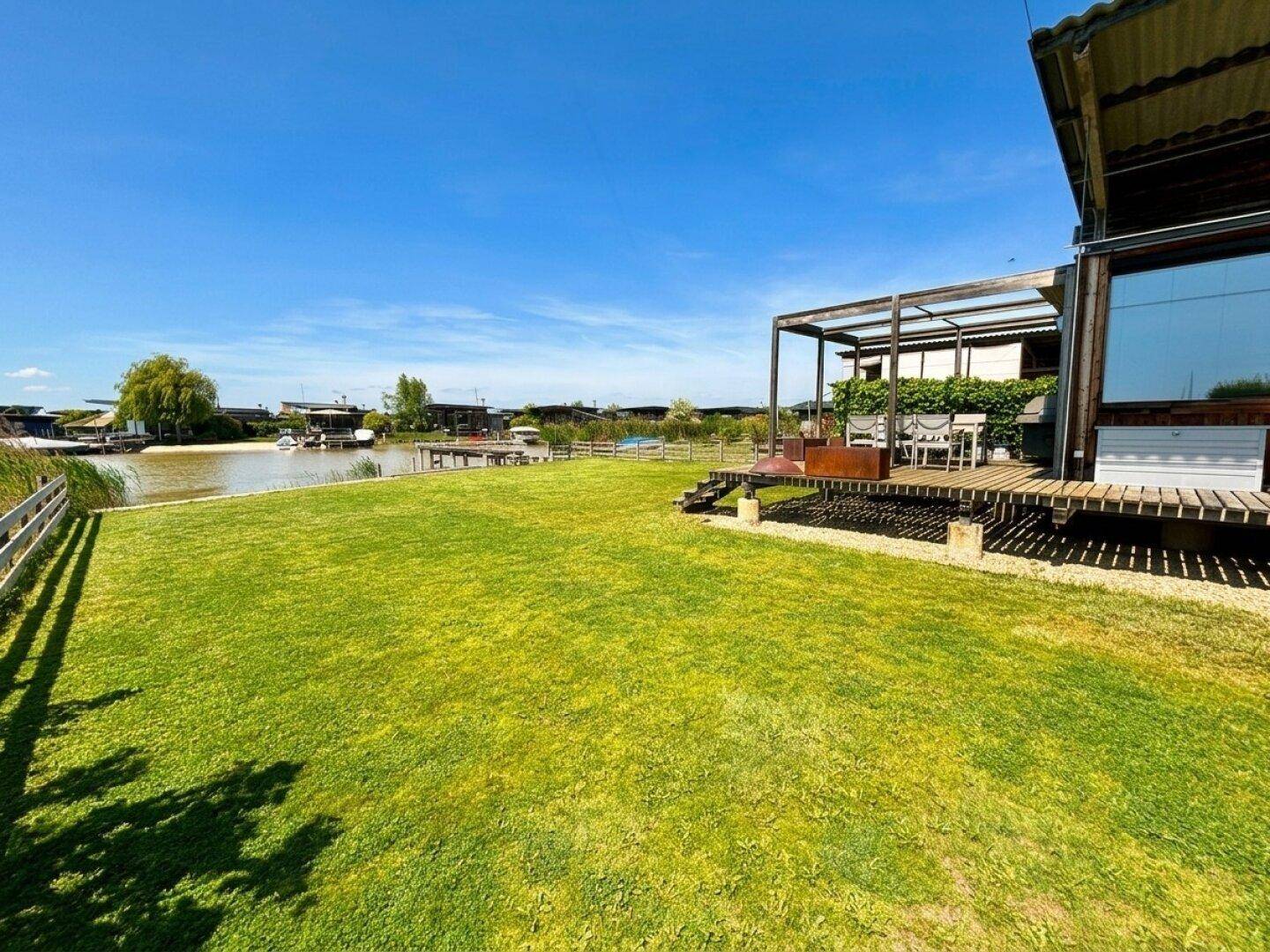 Großer Garten mit Rasenfläche und Holzterrasse mit Sitzgelegenheiten und Blick auf den See.