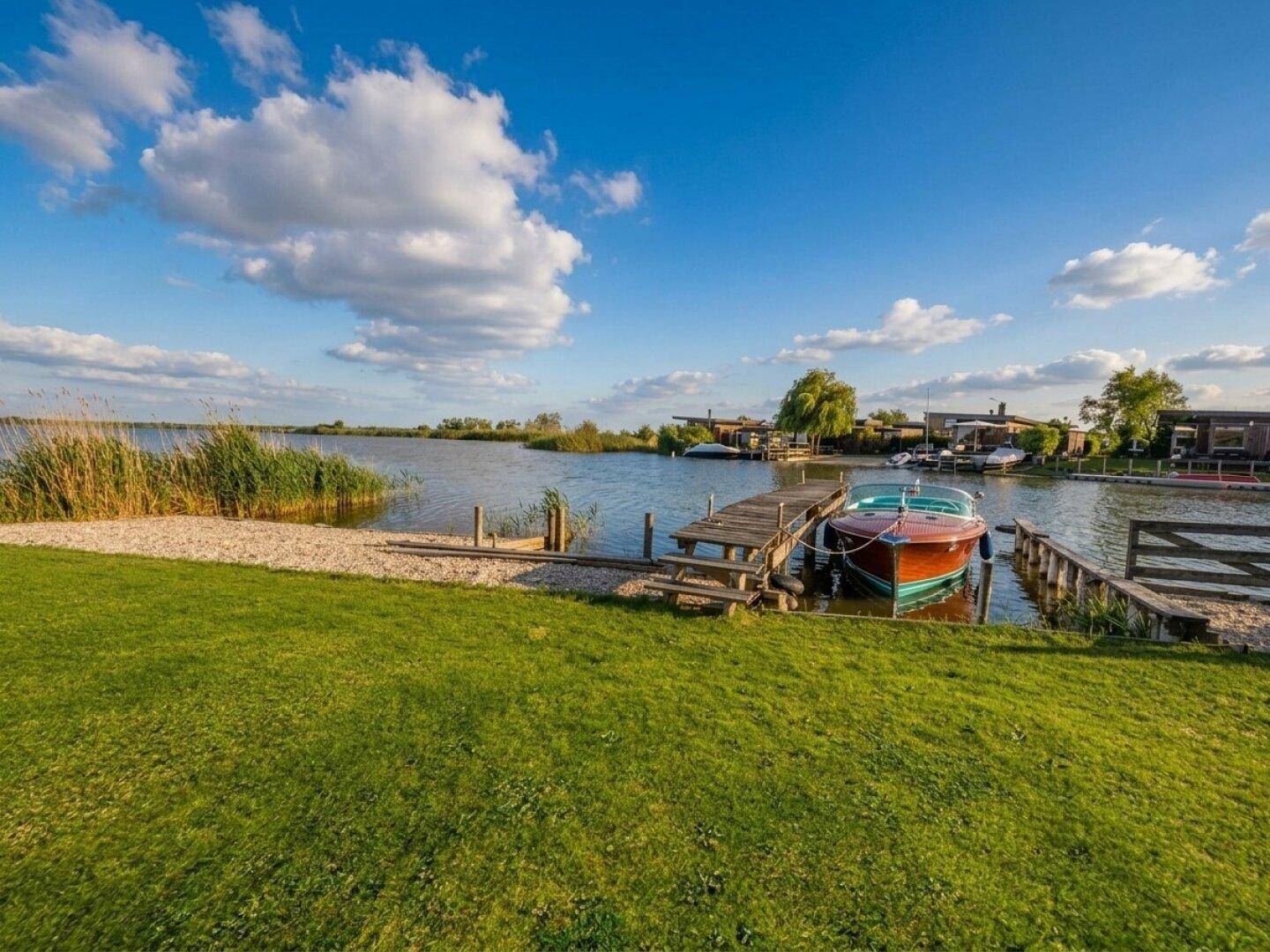 Weitläufiger Garten mit direktem Seezugang und privatem Bootssteg unter blauem Himmel.