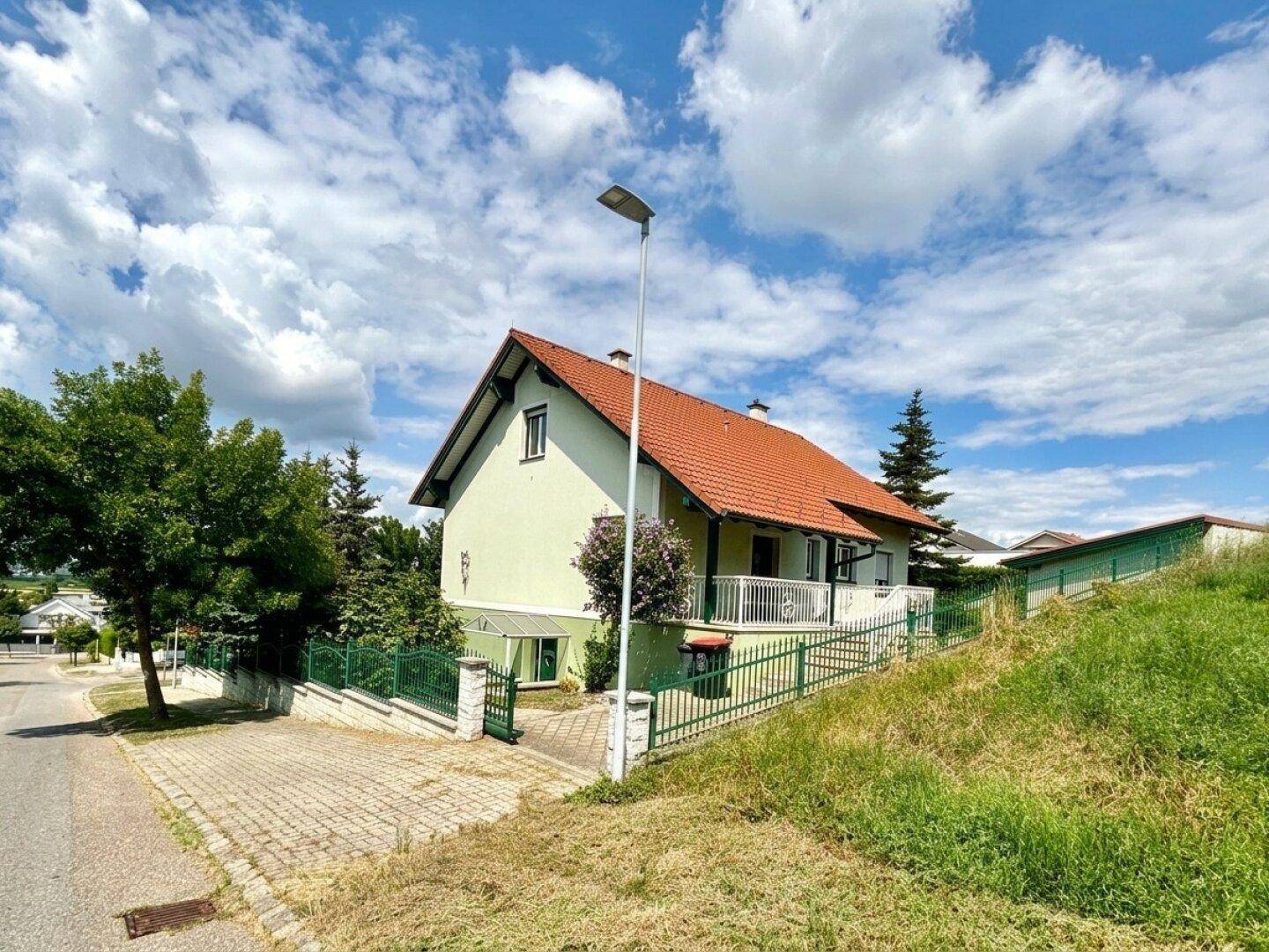 Einfamilienhaus mit hellgrüner Fassade, rotem Ziegeldach und kleinem Vorgarten.