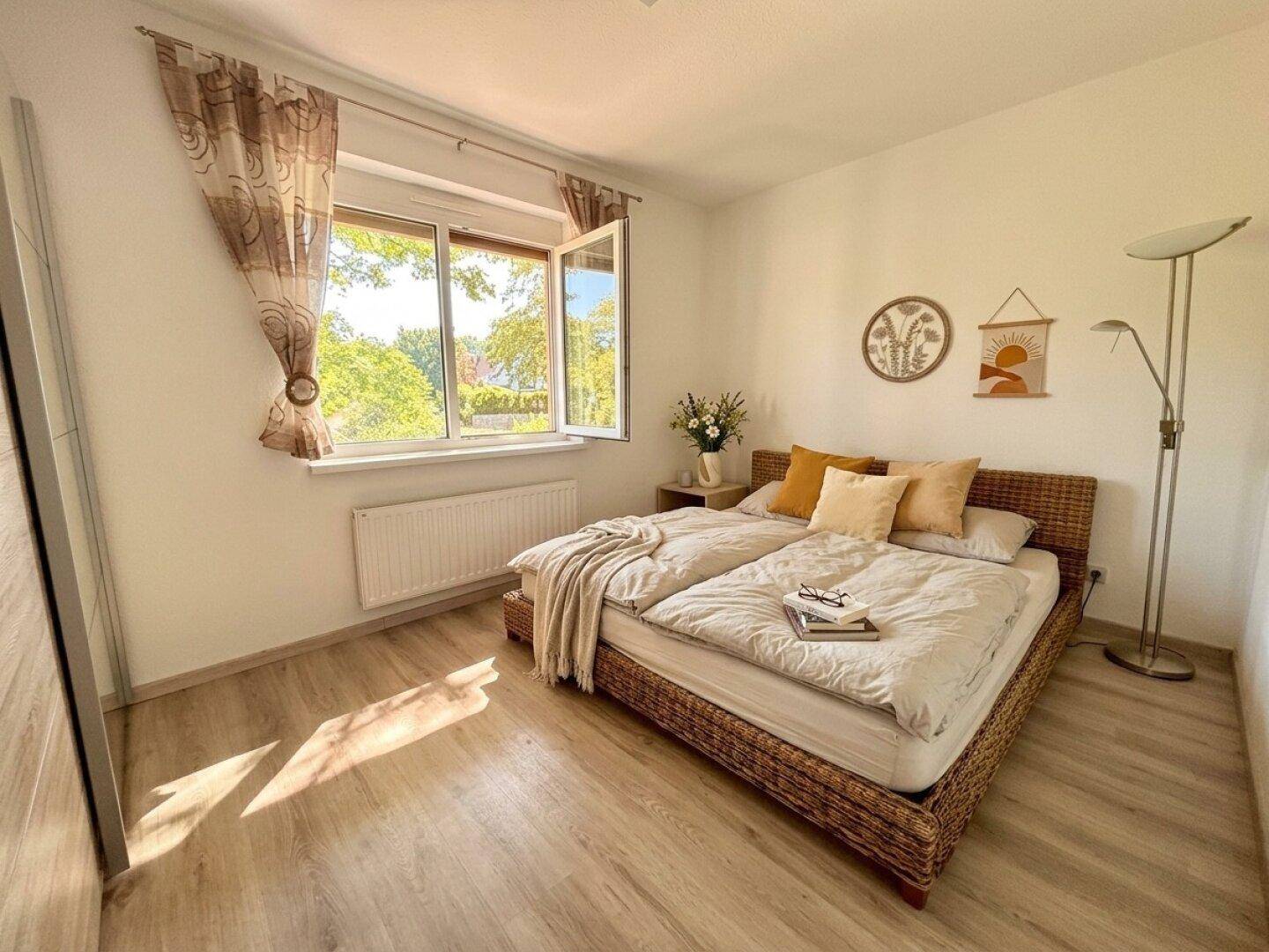 Helles Schlafzimmer mit Doppelbett, Laminatboden und Blick ins Grüne.