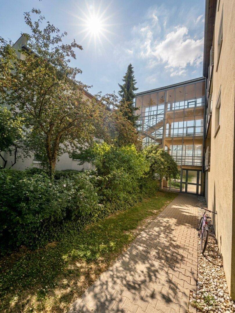 Außenansicht des Gebäudes mit viel Grün und einem verglasten Treppenhaus.
