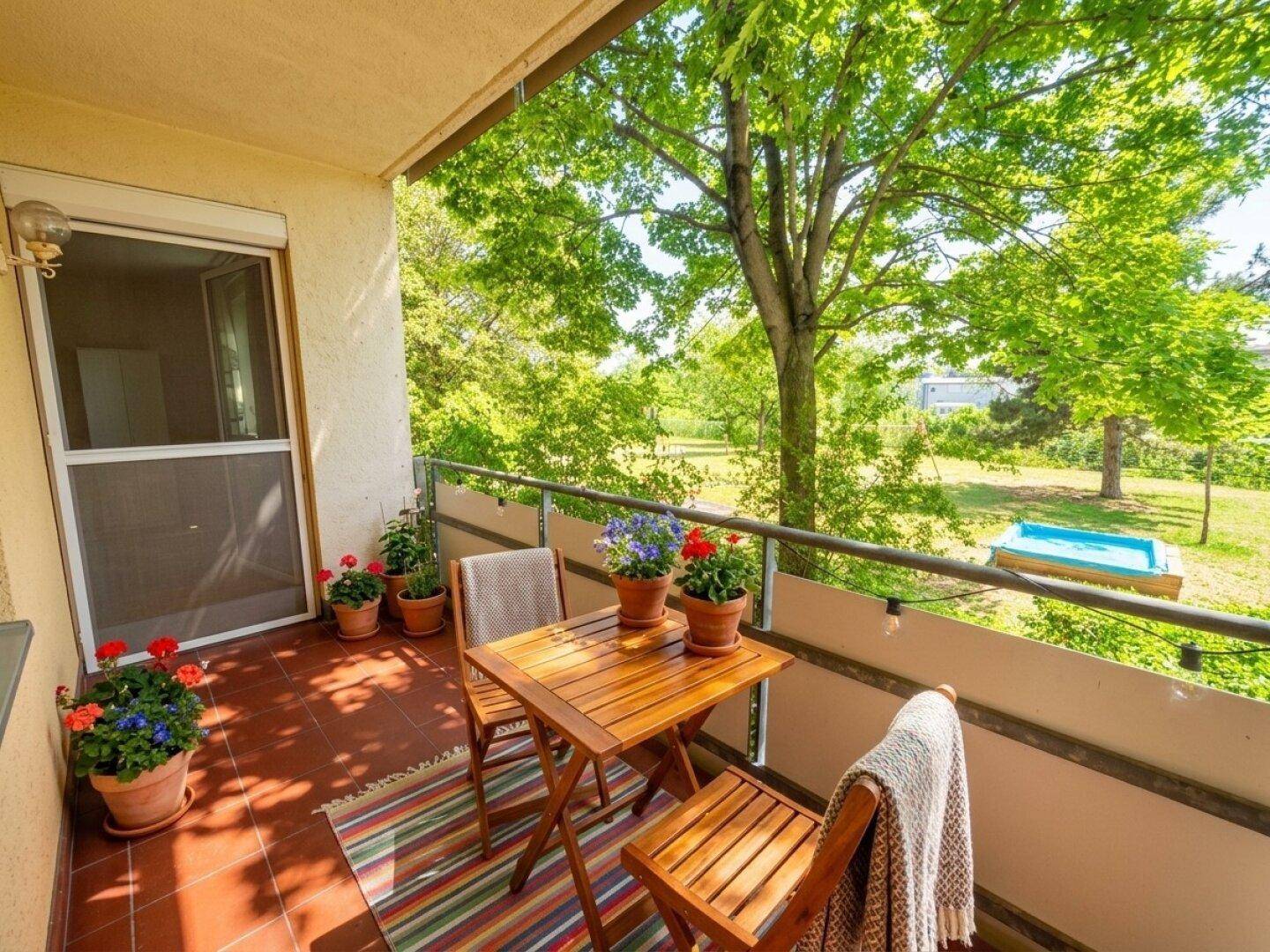 Sonniger Balkon mit Terracotta-Fliesen, Sitzgelegenheiten und Blick ins Grüne.