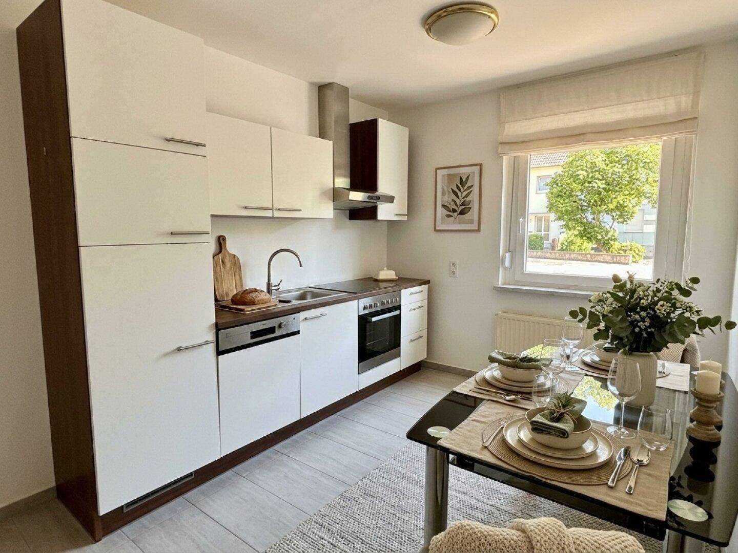Moderne Küche mit weißen Schränken, Essbereich und Fenster mit Blick ins Grüne.
