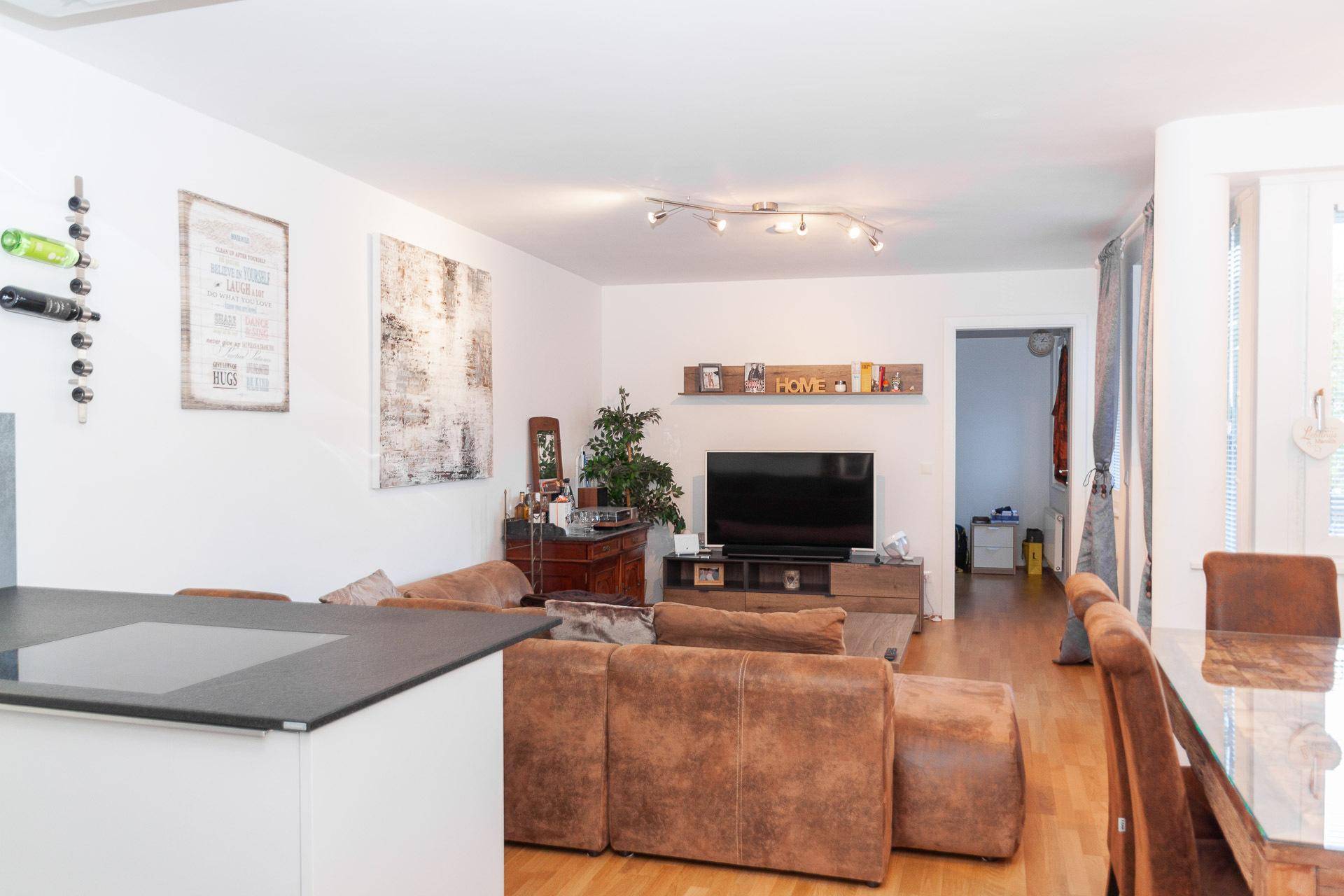 Heller Wohnbereich mit bequemer Couch, Holzboden und Blick auf den Essbereich und die Küche.