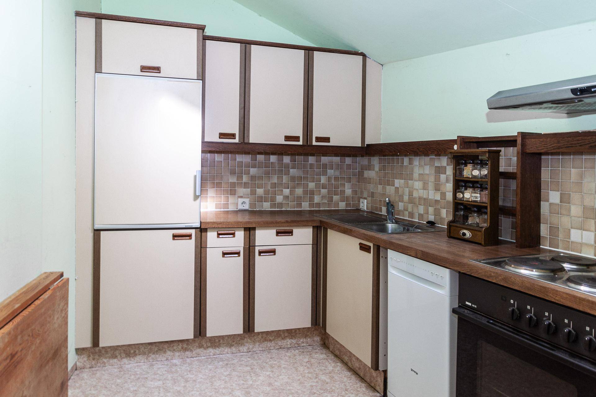 Ältere Einbauküche mit beigen Schränken, Spülmaschine und Herd, bereit zur Modernisierung.