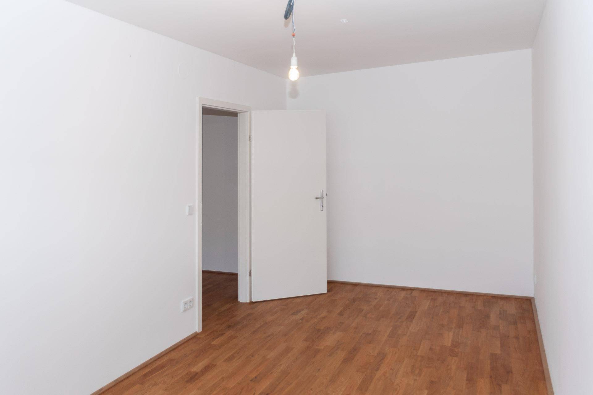 Schlafzimmer mit Holzboden, weißen Wänden und einer Tür, die zu einem weiteren Raum führt.