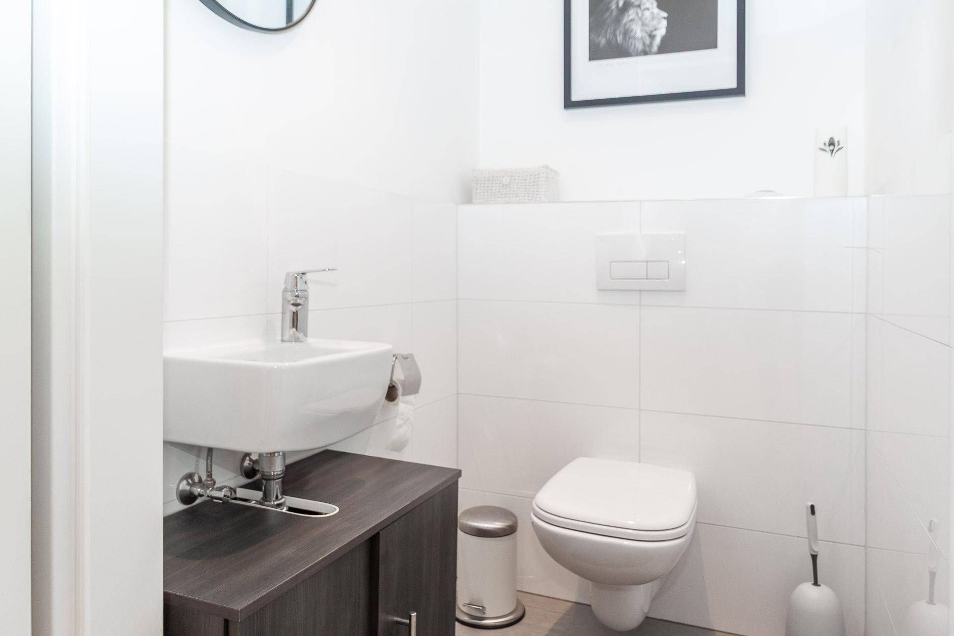 Modernes Gäste-WC mit wandhängender Toilette, kleinem Waschbecken und schlichtem Design.