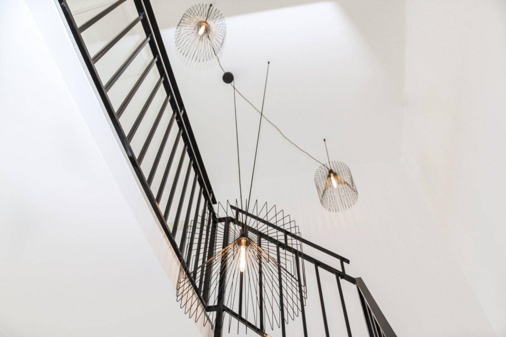 Elegantes Treppenhaus mit modernem schwarzen Geländer und dekorativen Hängelampen.