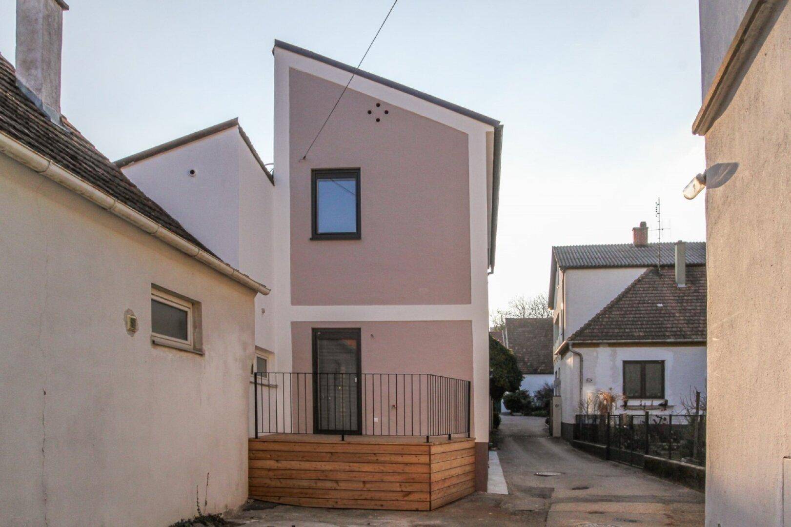 Rückansicht des Gebäudes mit moderner Architektur, Holzterrasse und Zugang zum Gartenbereich.