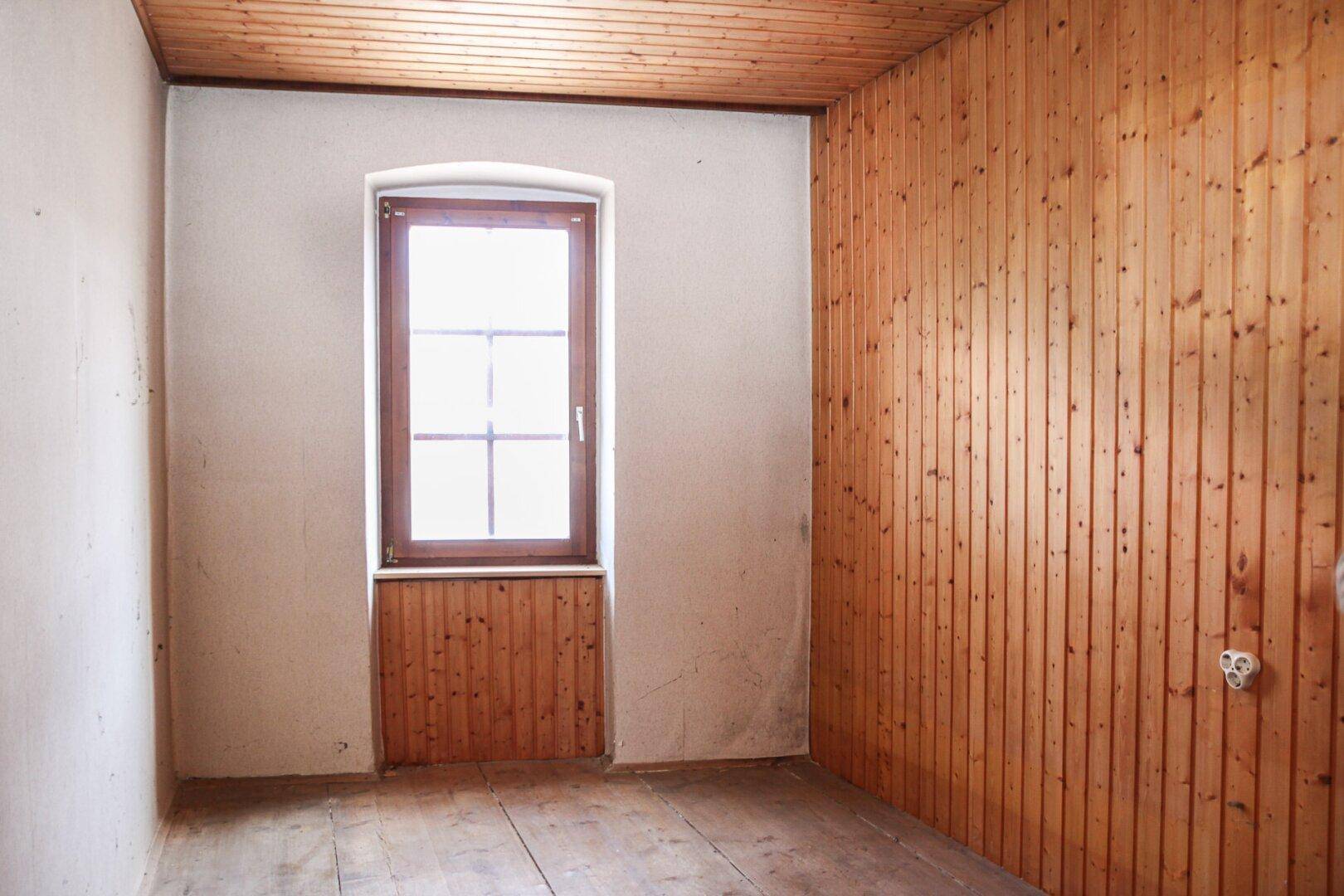 Kleiner Raum mit Holzbalkendecke und Holzvertäfelung an einer Wand, mit einem Fenster.