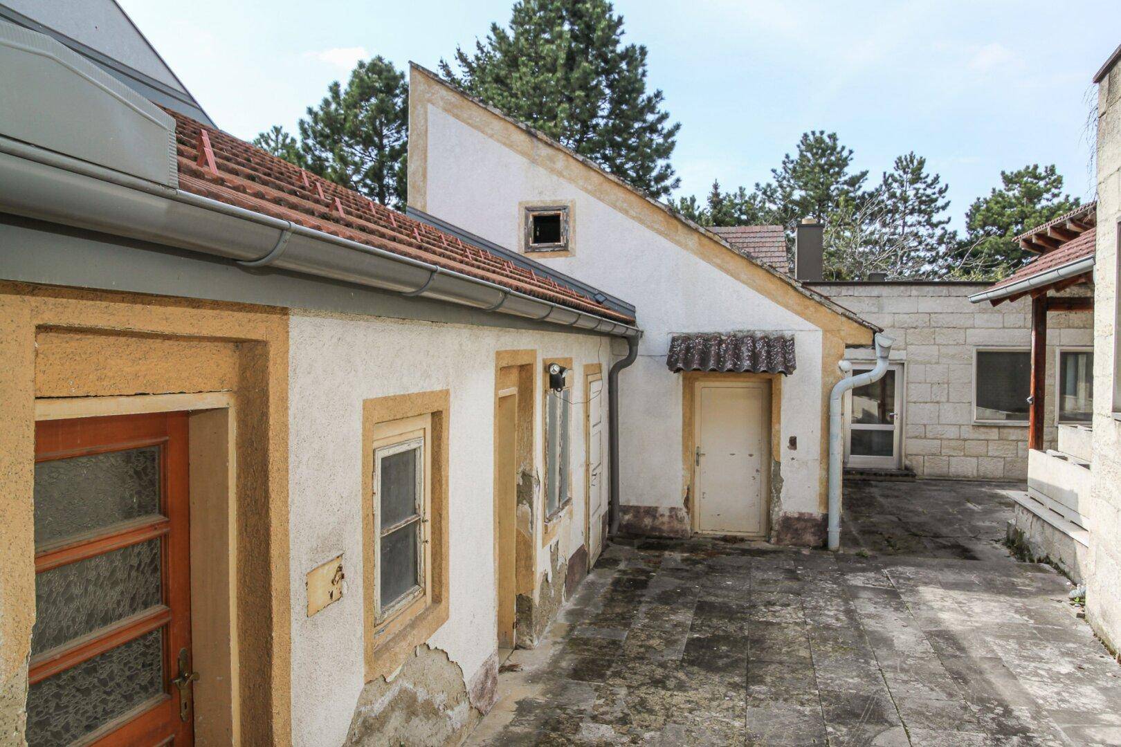 Hinterhofbereich mit gepflastertem Boden, alten Gebäudefassaden und Bäumen im Hintergrund.