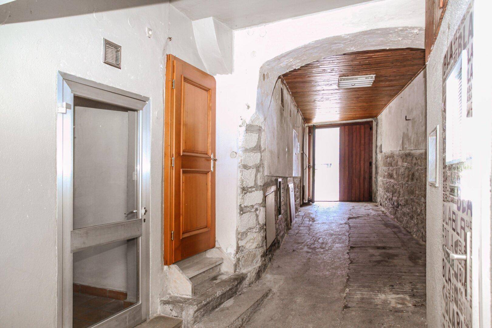 Langer, schmaler Flur mit gewölbter Decke, Holztüren und abgenutzten Steinwänden.