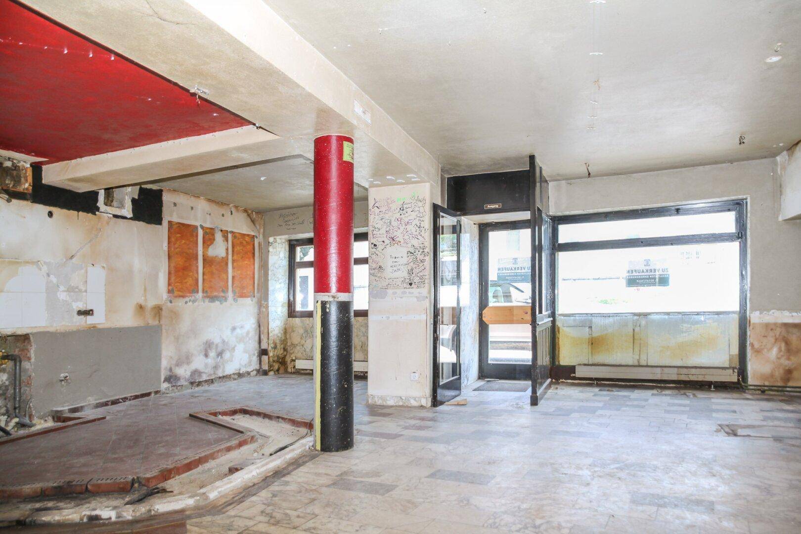 Großer, leerer Raum mit abgenutzten Wänden, Säulen und großen Fenstern zur Straße.